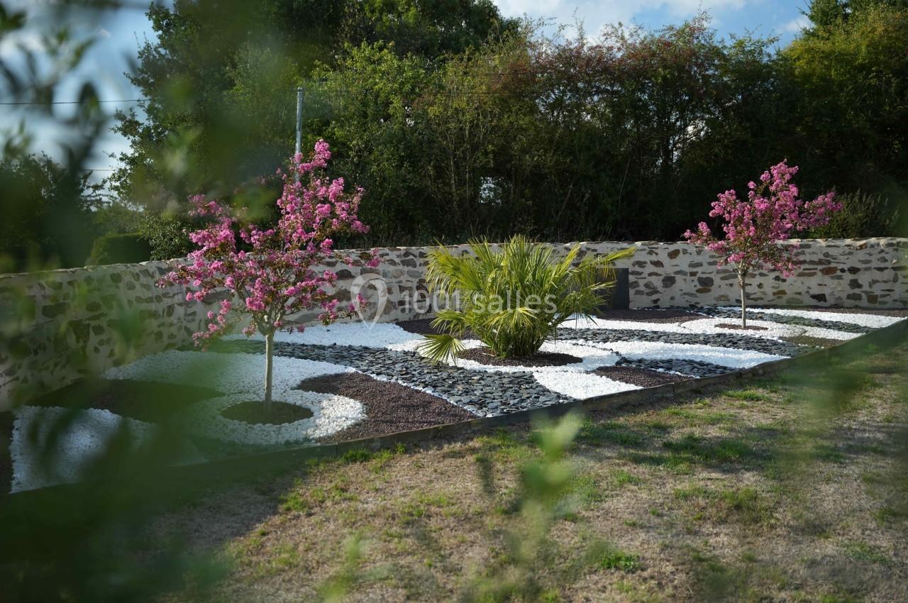 Jardin paysager avec deux arbres en fleurs, un palmier central et des motifs de gravier blanc et noir.