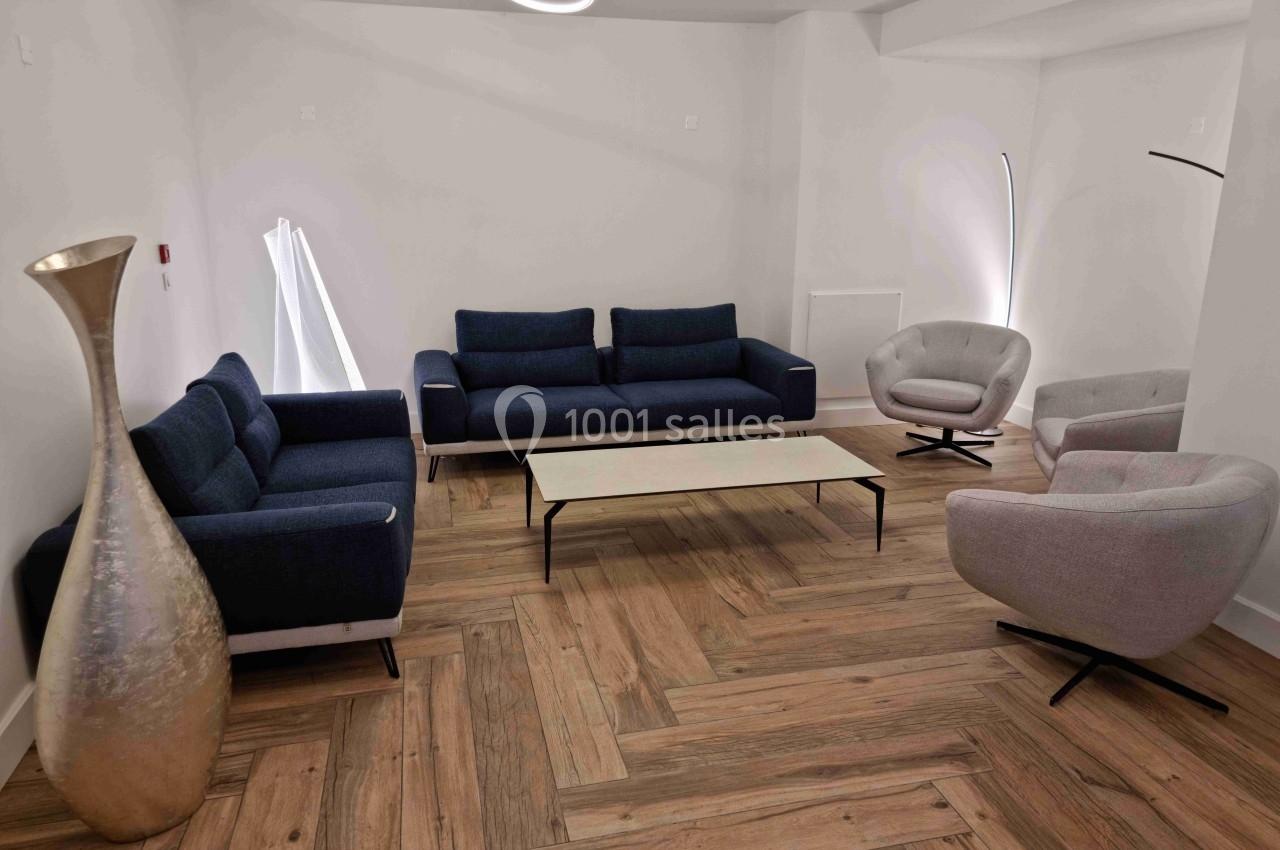 Salon moderne avec deux canapés bleus, deux fauteuils gris, une table basse blanche et un sol en bois clair.