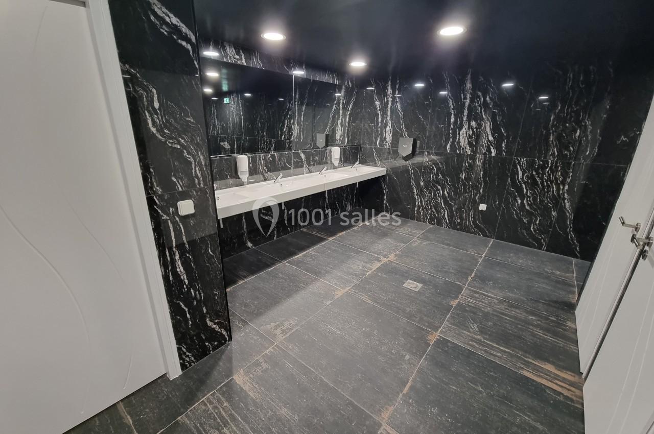 Salle de bain moderne avec murs et sol en marbre noir, équipée de lavabos et d'un grand miroir.