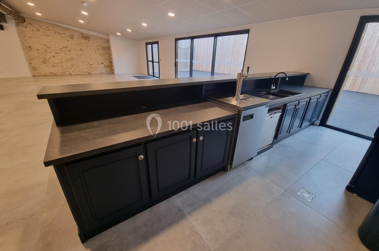 Cuisine moderne avec îlot central noir, plan de travail en pierre, évier inox et lave-vaisselle, dans une pièce lumineuse.