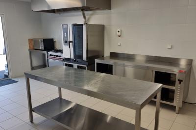 Cuisine professionnelle avec évier en inox, lave-vaisselle industriel, chariots noirs et casiers empilés sur sol carrelé.