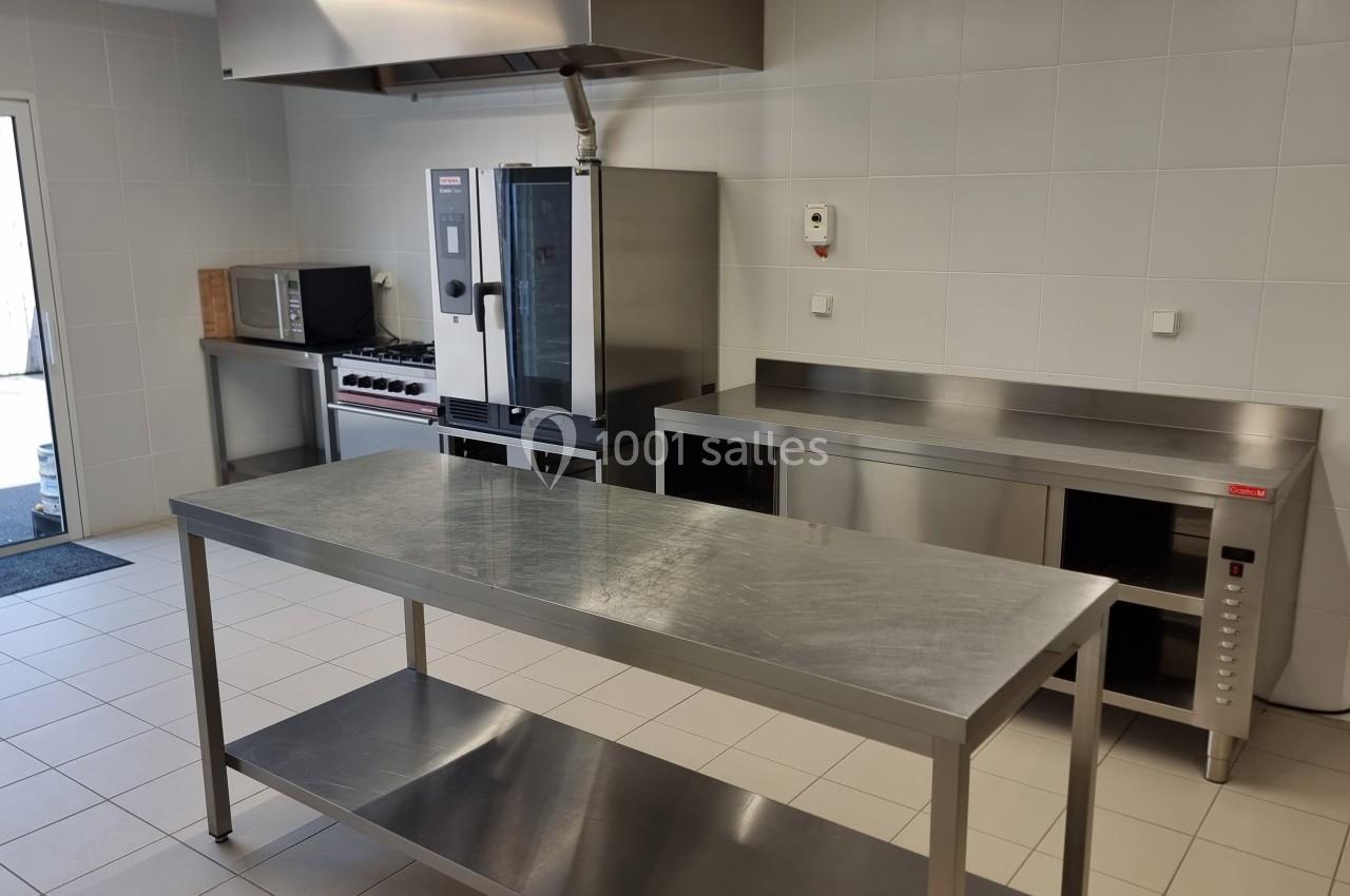 Cuisine professionnelle avec plan de travail en inox, four, micro-ondes et équipements sur fond de murs carrelés blancs.