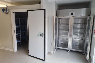 Cuisine professionnelle avec évier en inox, lave-vaisselle industriel, chariots noirs et casiers empilés sur sol carrelé.