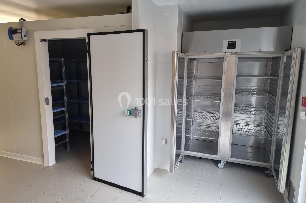 Chambre froide ouverte avec étagères métalliques et armoire réfrigérée en acier inoxydable dans une pièce carrelée.