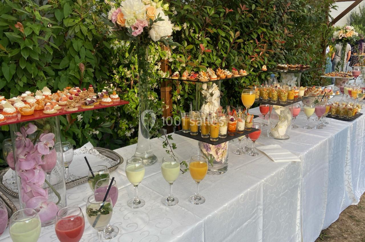 Buffet en extérieur avec verrines, cocktails colorés et petits fours, décoré de fleurs et entouré de verdure.