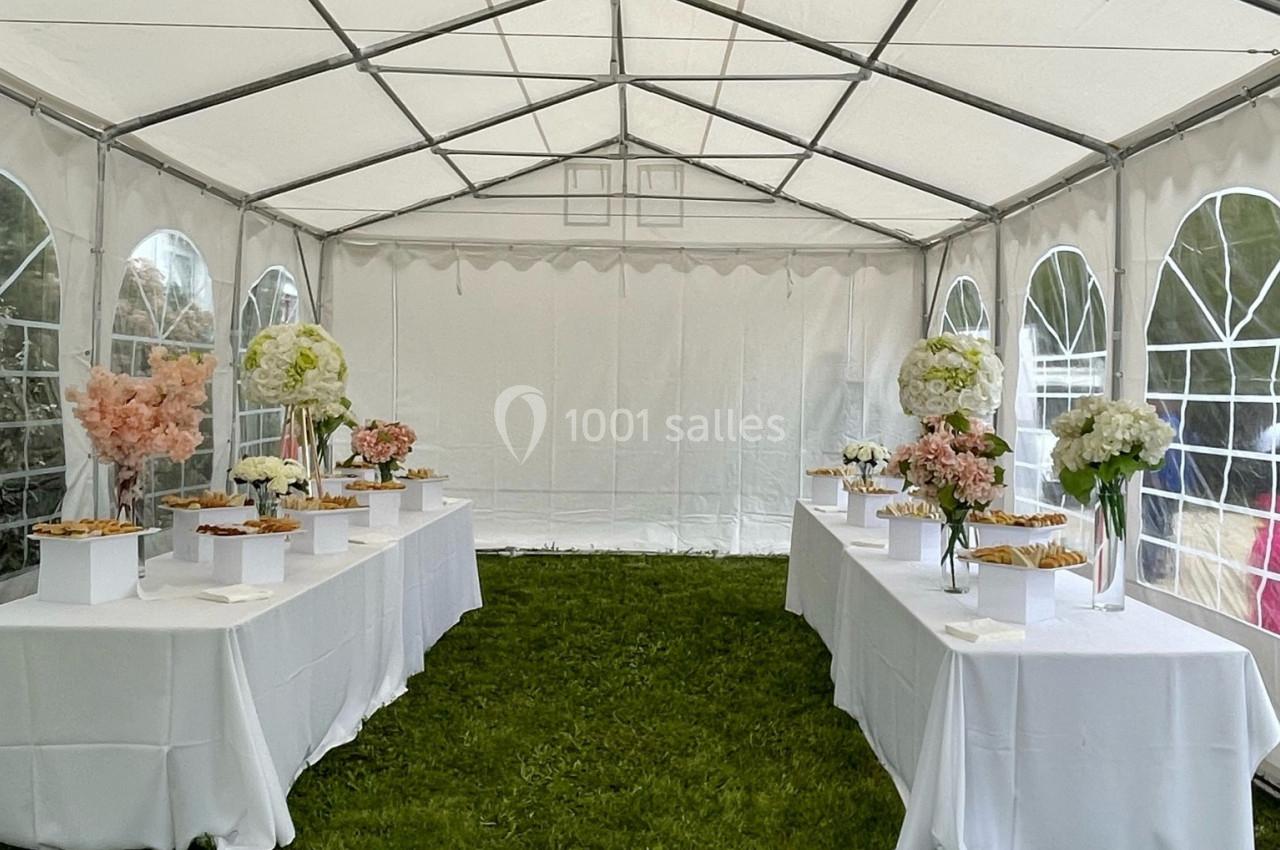 Intérieur d'une tente blanche avec des tables décorées de fleurs et de plats, posées sur une pelouse verte.