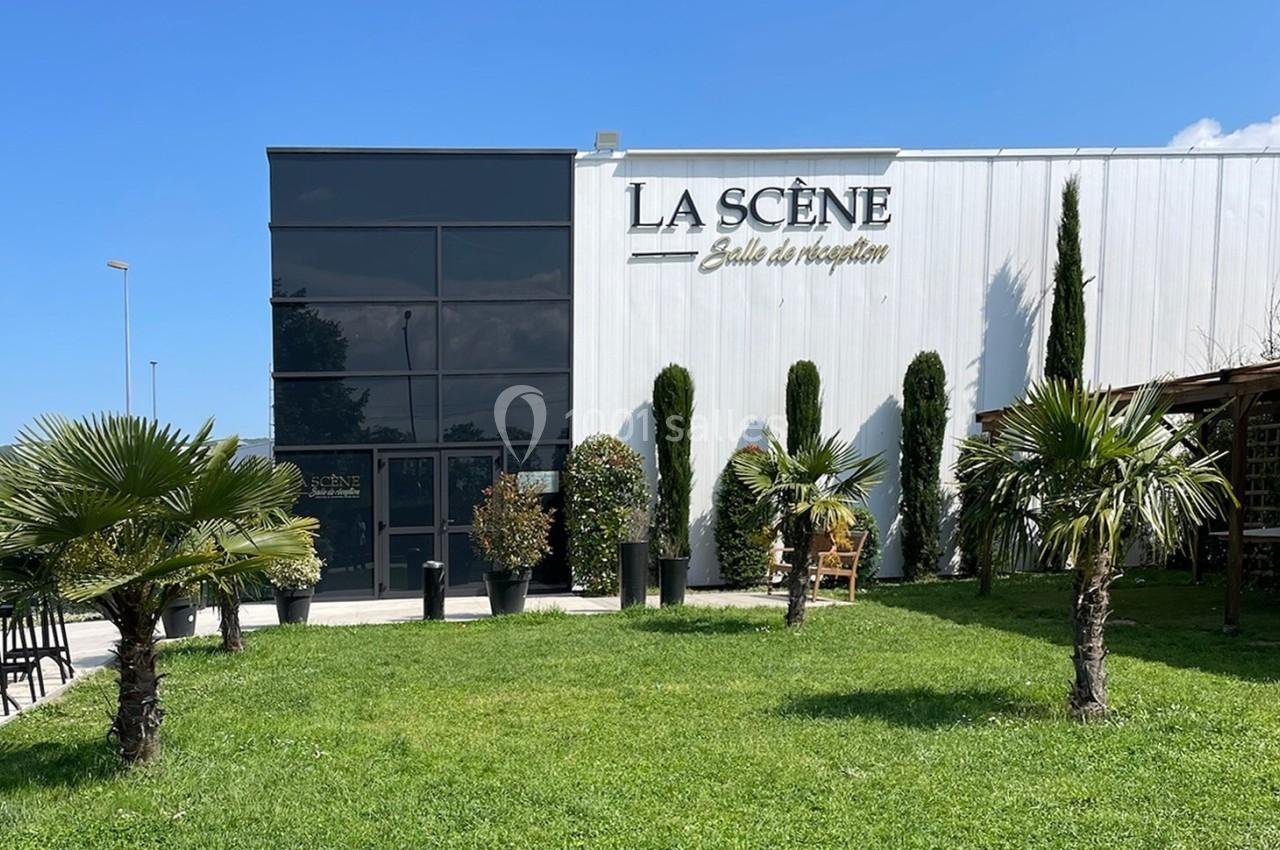 Façade d'une salle de réception moderne avec pelouse, palmiers et arbustes devant l'entrée vitrée.