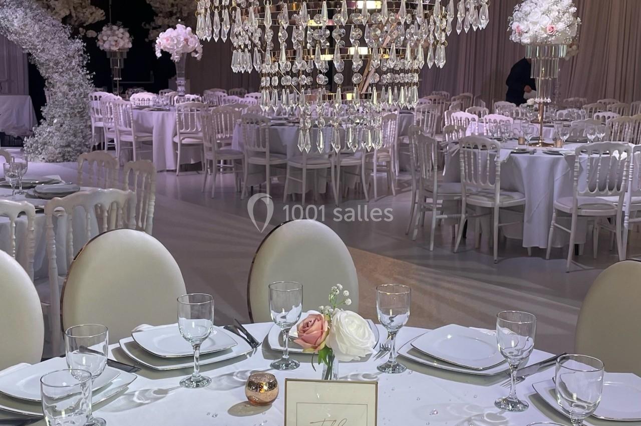 Salle de réception élégante avec tables dressées, grand lustre en cristal et décoration florale blanche.