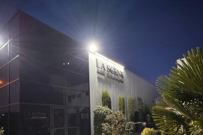 Façade d'un bâtiment moderne éclairé de nuit, avec des plantes et un panneau ’La Scène’ visible.