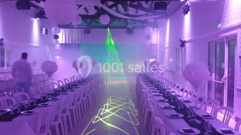 Salle de réception décorée avec des tables alignées, éclairage violet et effets de lumière laser verts.