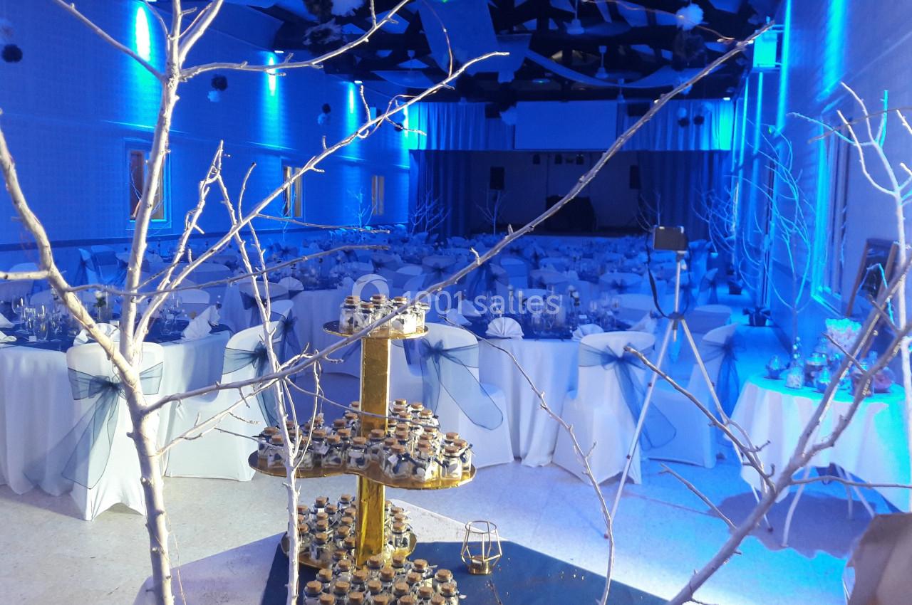 Salle de réception décorée en bleu avec tables dressées et un présentoir doré de desserts au premier plan.