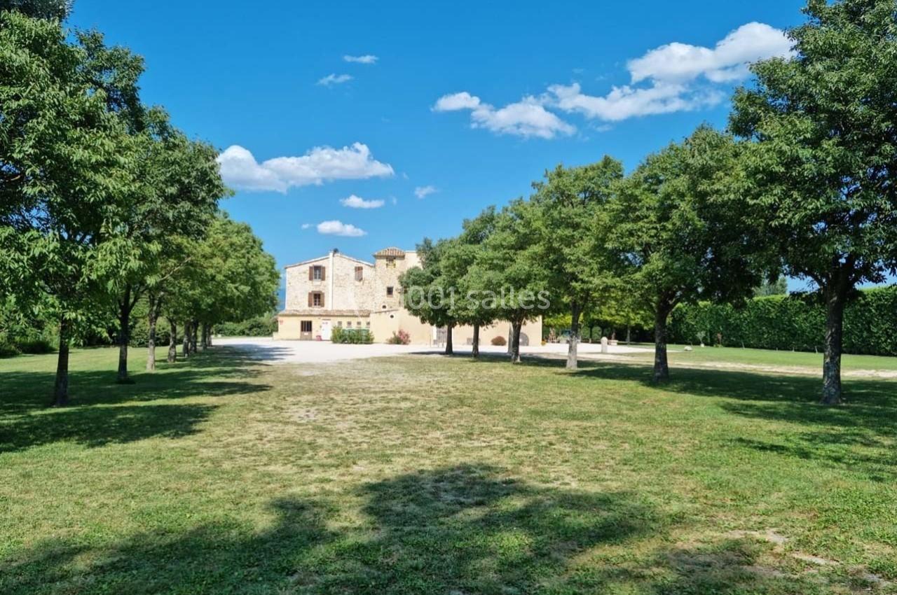 Allée bordée d'arbres menant à une maison en pierre sous un ciel bleu dégagé.