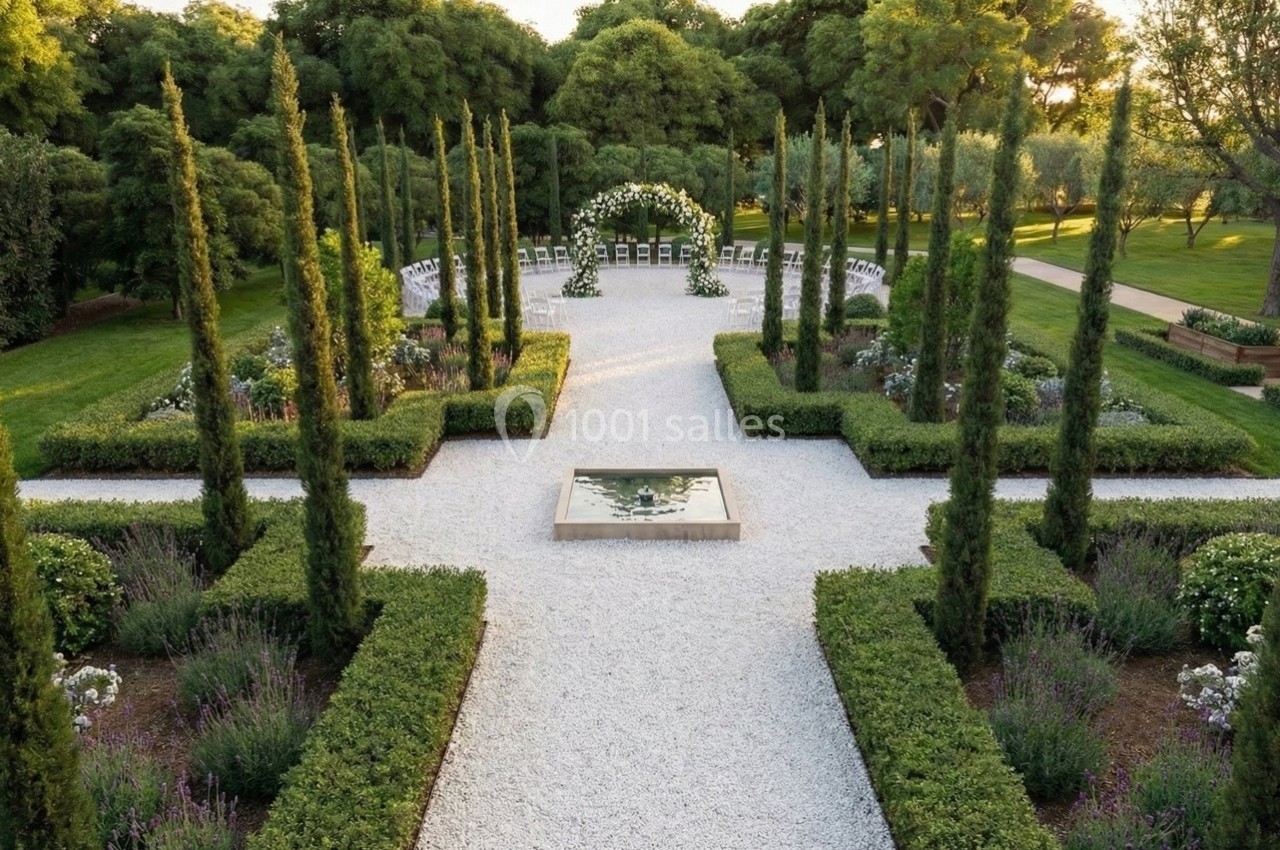 Allée bordée de cyprès menant à une arche fleurie dans un jardin paysager avec pelouse et parterres de fleurs.