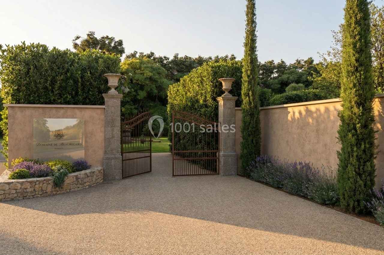Portail en fer forgé ouvert, entouré de murs en pierre, de lavandes et de cyprès, donnant sur un jardin verdoyant.