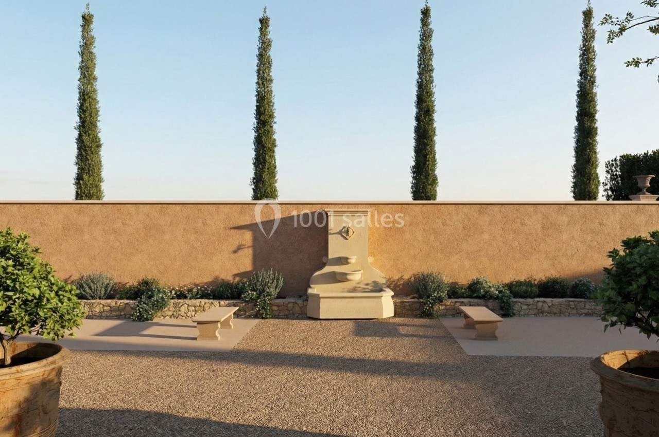 Cour extérieure avec fontaine centrale, bancs en pierre, cyprès alignés et végétation méditerranéenne.