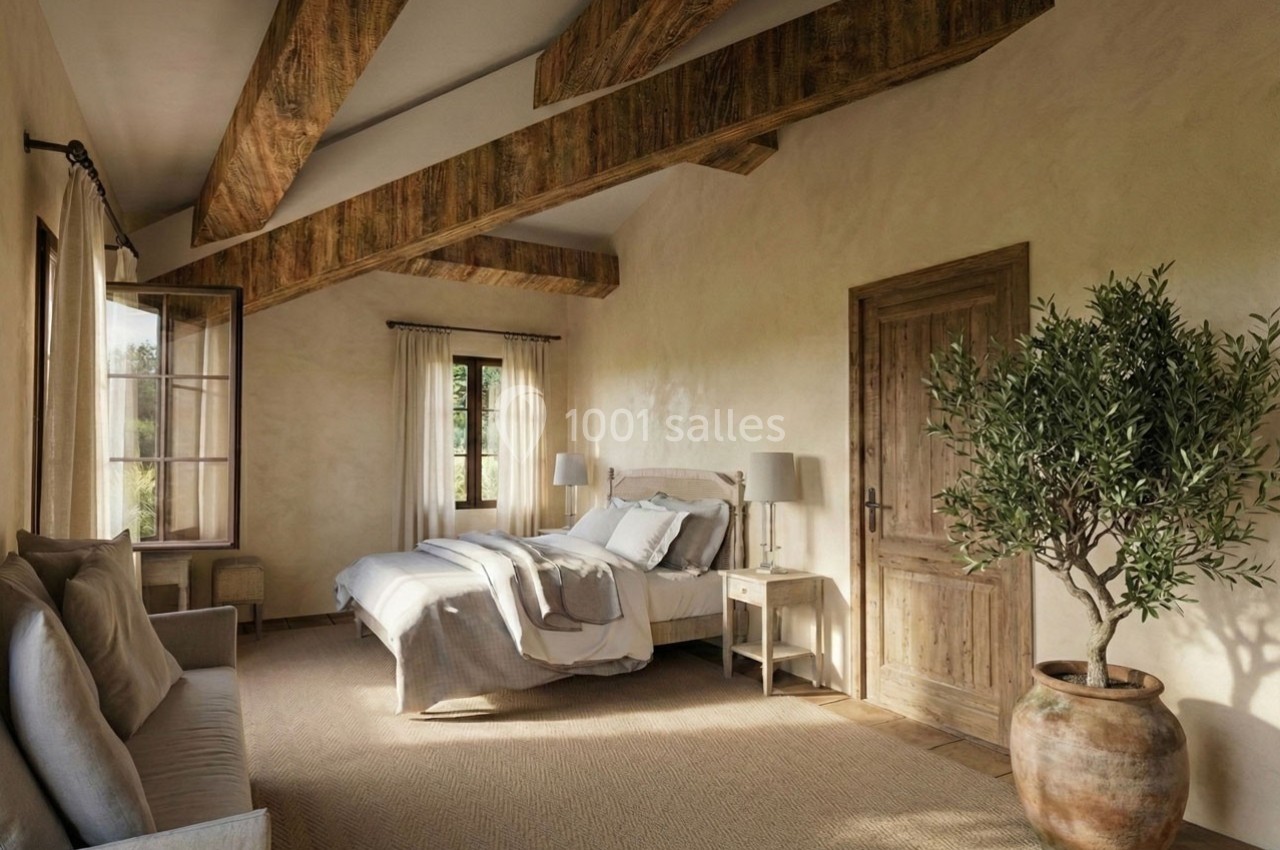 Chambre lumineuse avec lit double, poutres apparentes, canapé, grandes fenêtres et un olivier en pot.