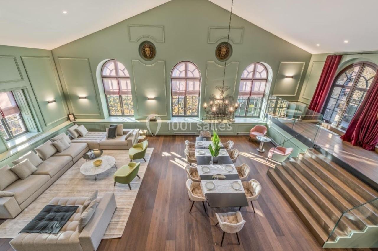 Salle de séjour spacieuse avec canapé, table à manger, lustre et grandes fenêtres cintrées laissant entrer la lumière.
