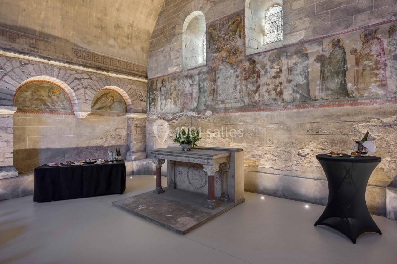 Autel en pierre dans une salle voûtée ornée de fresques murales, avec des tables dressées pour un événement.