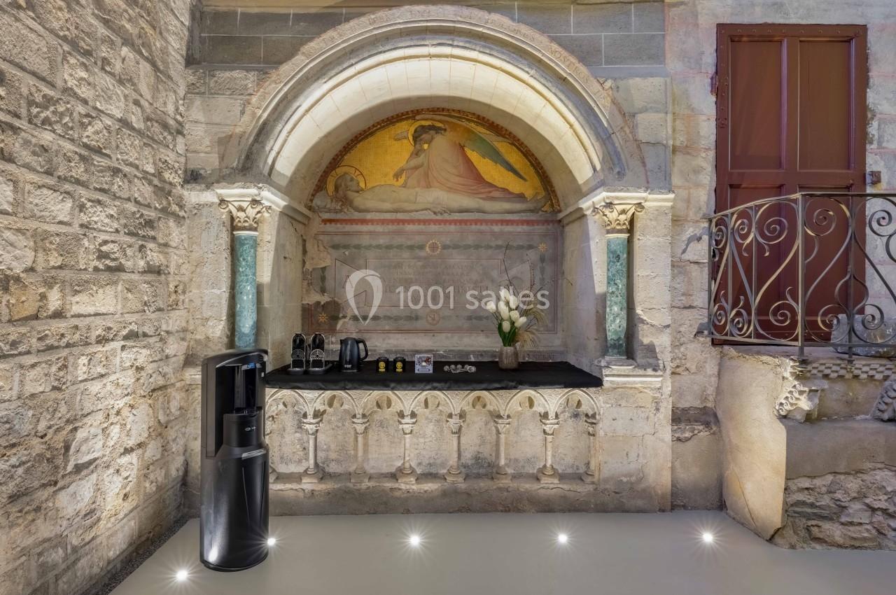 Un coin café moderne installé dans une alcôve en pierre ancienne avec une fresque et des colonnes décoratives.