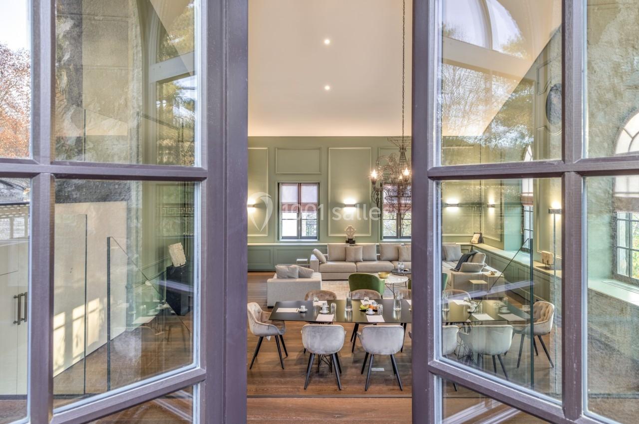 Vue à travers une porte vitrée sur une salle lumineuse avec table à manger, chaises et canapé dans un décor élégant.