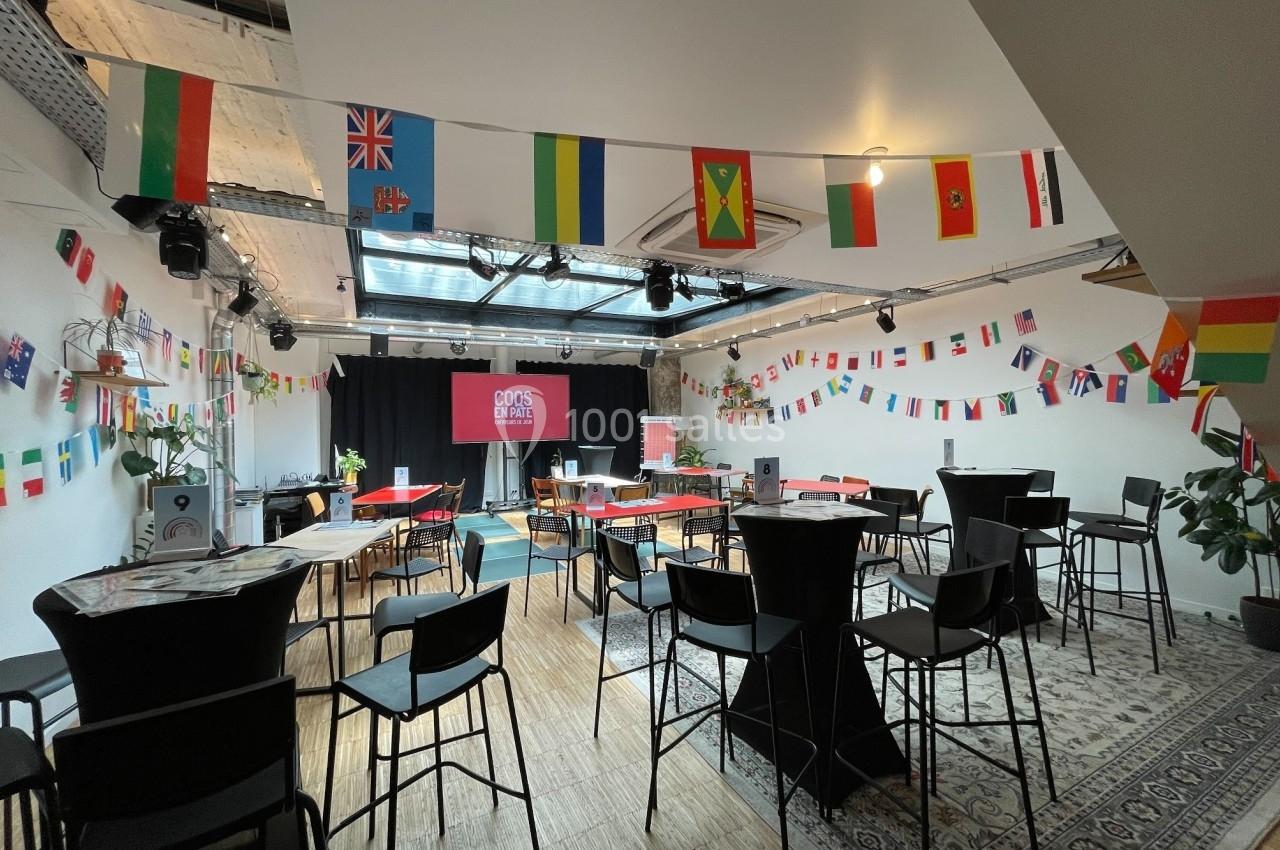 Salle décorée de drapeaux internationaux, aménagée avec des tables hautes et des chaises pour un événement.