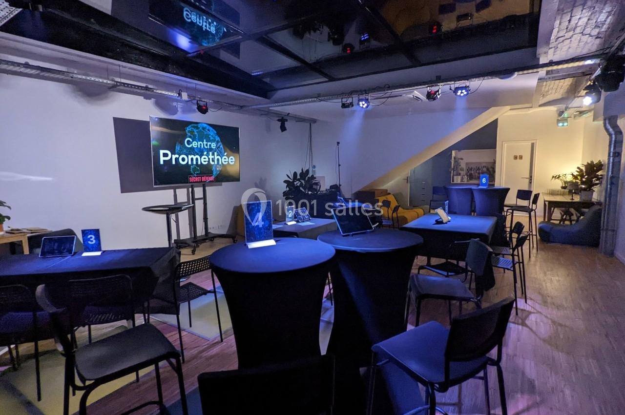 Salle de conférence moderne avec tables hautes, chaises, écrans et éclairage tamisé.