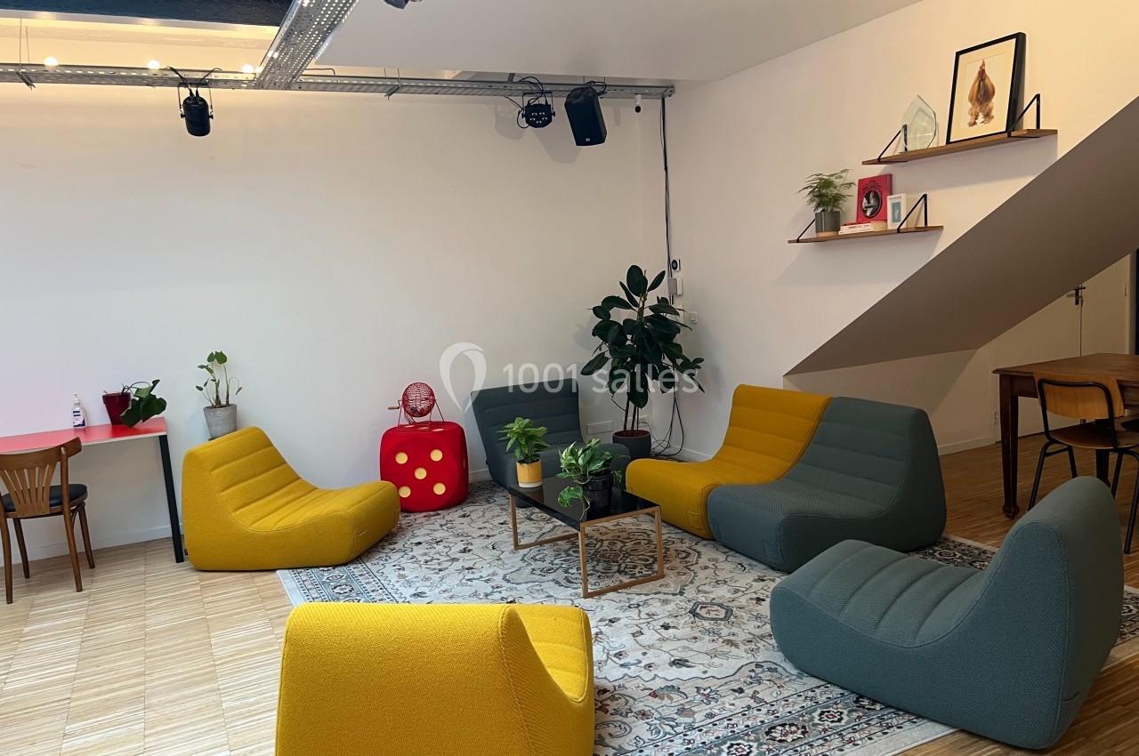 Espace de détente avec fauteuils colorés, tapis, plantes et étagères décorées dans une pièce lumineuse.