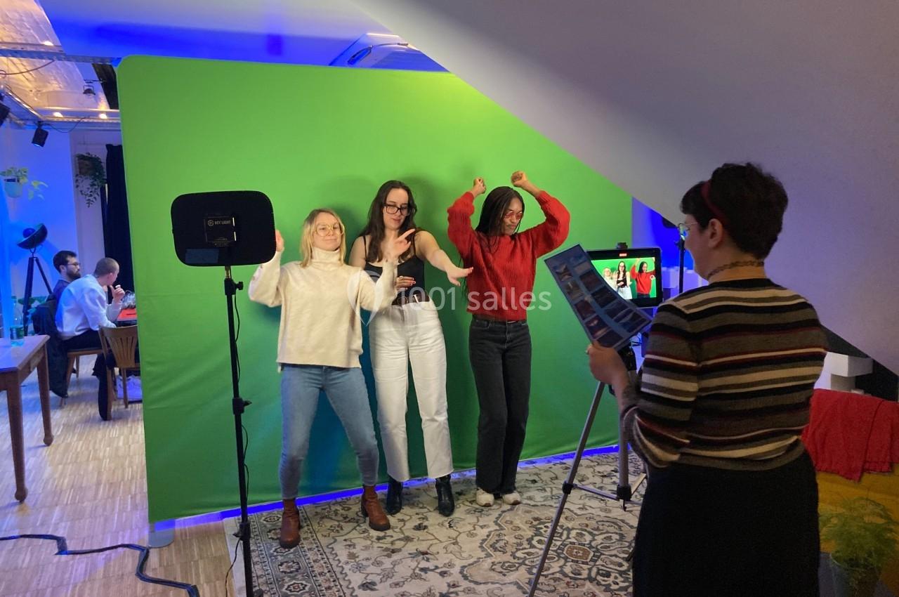 Trois personnes posent devant un fond vert, éclairées par des projecteurs, tandis qu'une autre les photographie.