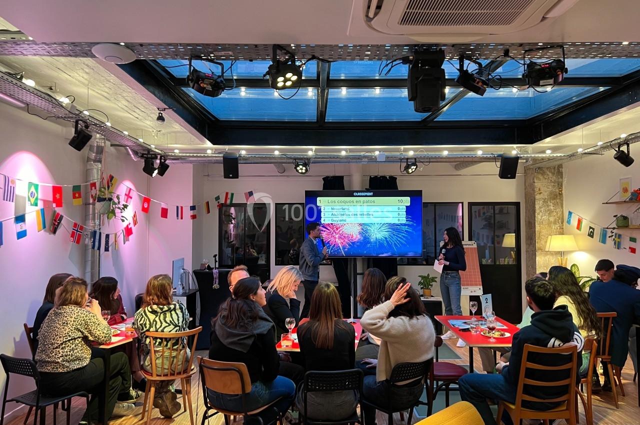 Un groupe de personnes assises dans une salle décorée de drapeaux, écoutant une présentation sur un écran.