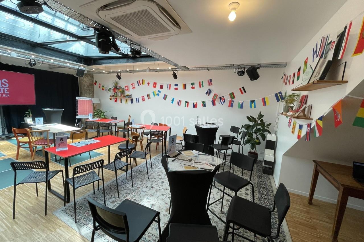 Salle lumineuse aménagée avec des tables, des chaises et des décorations de drapeaux internationaux suspendus.