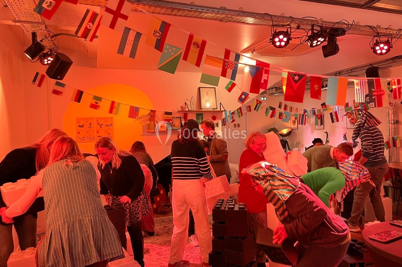 Des personnes assemblent des blocs dans une salle décorée de drapeaux internationaux et éclairée par des lumières colorées.