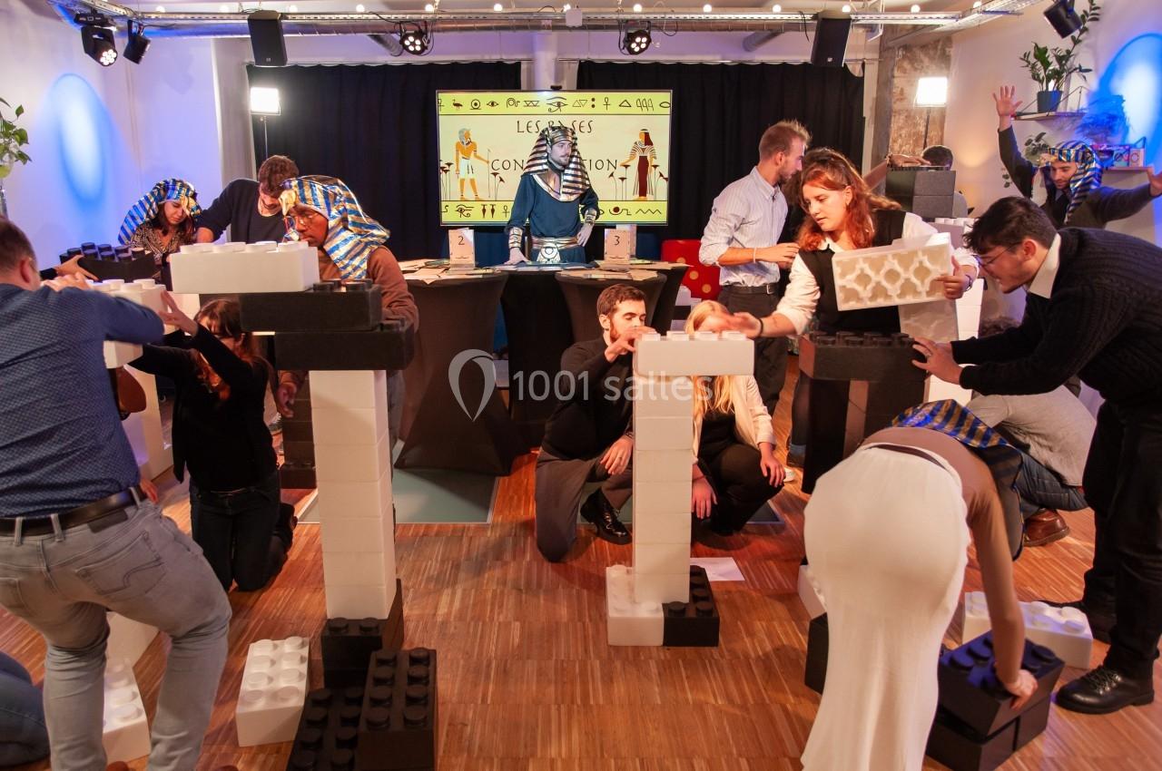 Des personnes construisent des structures avec de grands blocs en plastique dans une salle décorée sur le thème de l'Égypte.