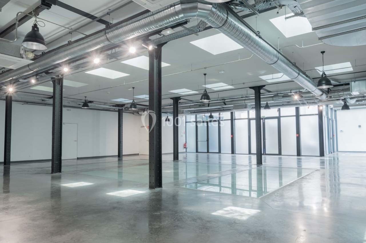 Intérieur d'un espace industriel moderne avec sol en béton, verrières, poutres métalliques et éclairage suspendu.