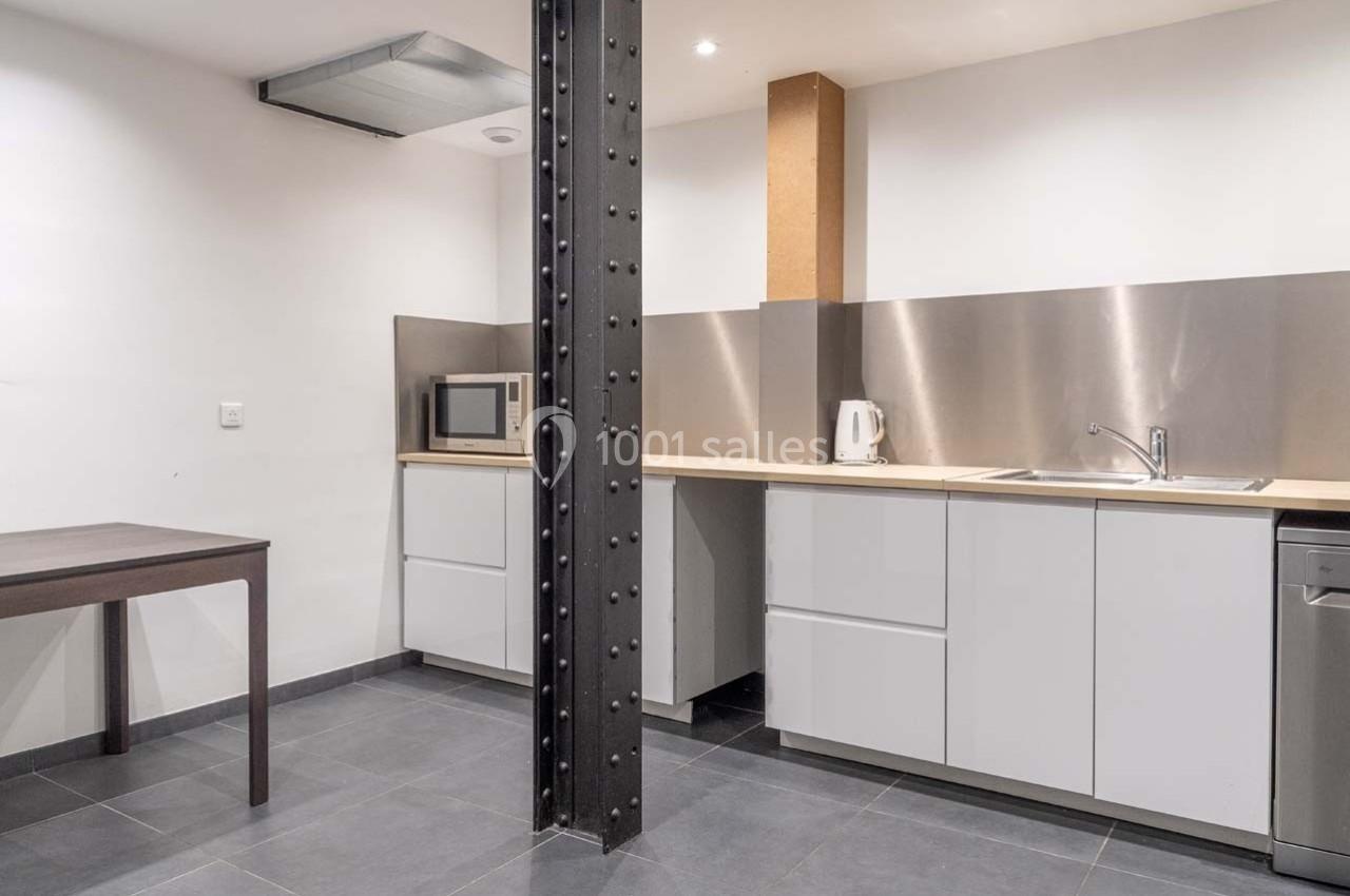 Cuisine moderne avec meubles blancs, plan de travail clair, évier en inox, micro-ondes et table en bois sombre.