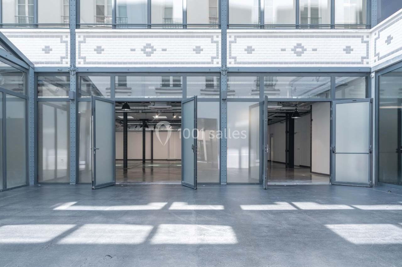 Vue d'un espace intérieur lumineux avec des portes vitrées ouvertes donnant sur une grande salle vide.