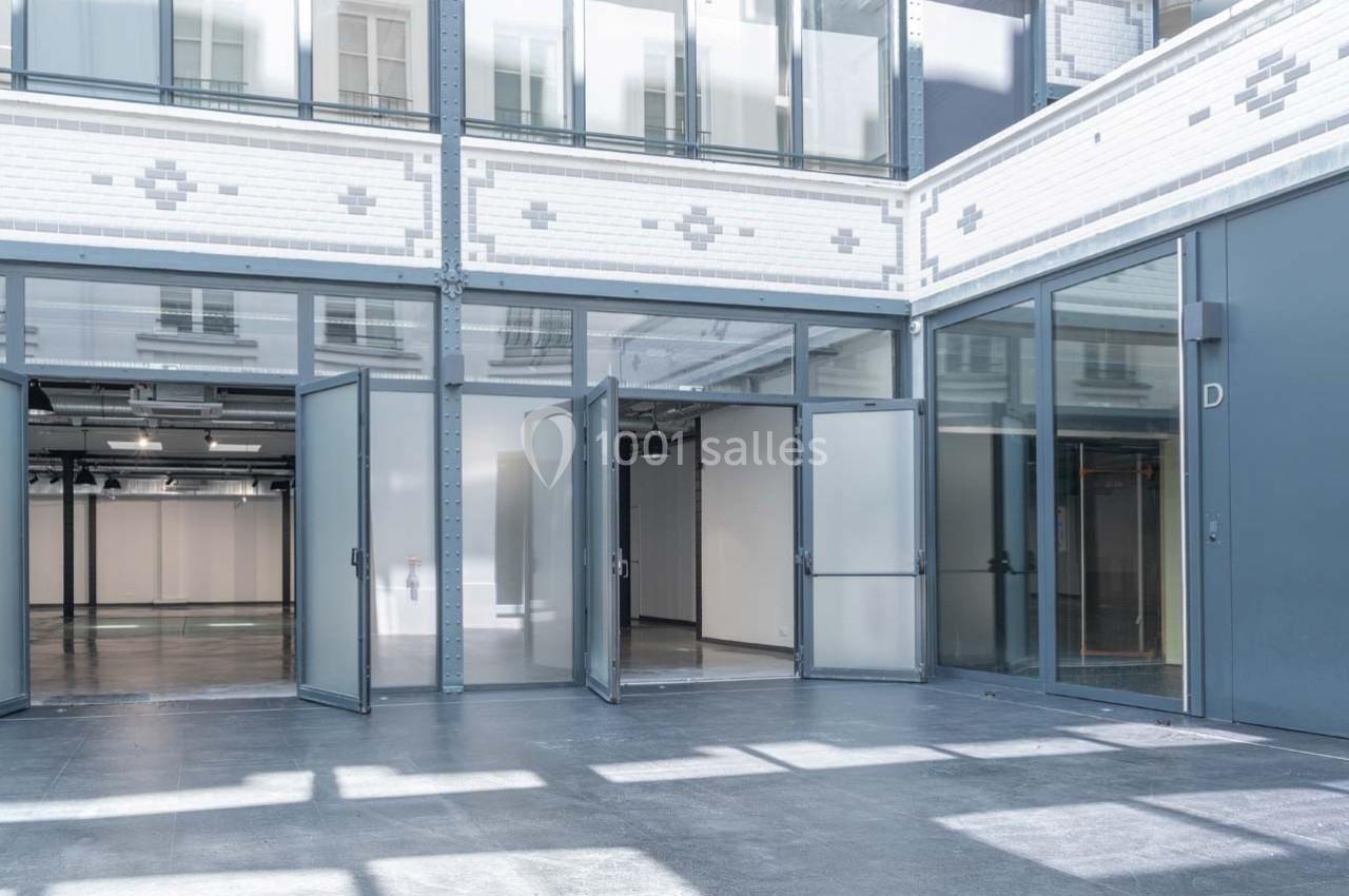 Façade vitrée d'un bâtiment moderne avec portes ouvertes donnant sur un espace intérieur lumineux.