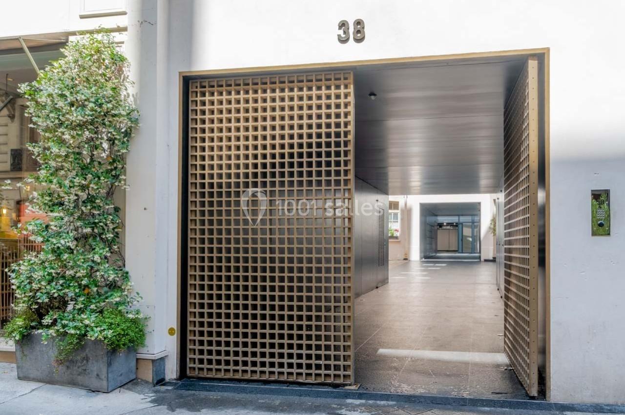 Entrée d'un bâtiment moderne avec une grille métallique dorée et un passage couvert menant à une cour intérieure.