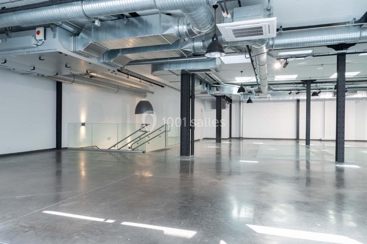 Intérieur d'un espace industriel moderne avec sol en béton, conduits apparents et escalier en verre.