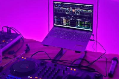 Poste de DJ avec ordinateur portable affichant un logiciel de mixage, platine et microphone sur une table éclairée en violet.