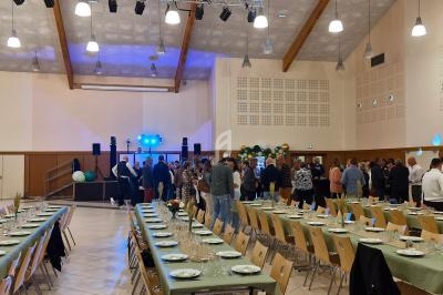 Salle de réception avec tables dressées et invités rassemblés près d'une piste de danse éclairée.