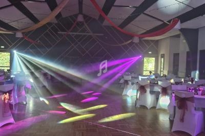 Salle de réception décorée avec des tables dressées, des rubans suspendus et des jeux de lumière colorés.