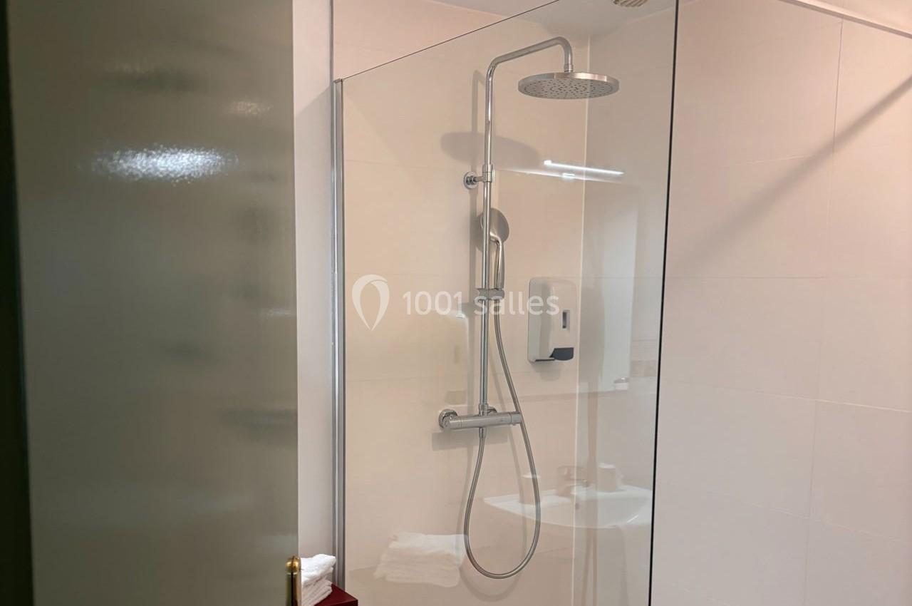 Douche moderne avec paroi vitrée, pommeau de pluie et distributeur de savon fixés sur un mur blanc.