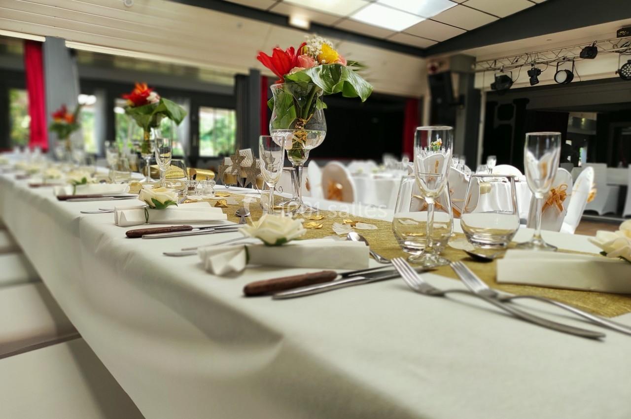 Table de réception élégamment dressée avec nappes blanches, fleurs colorées et couverts alignés dans une salle lumineuse.