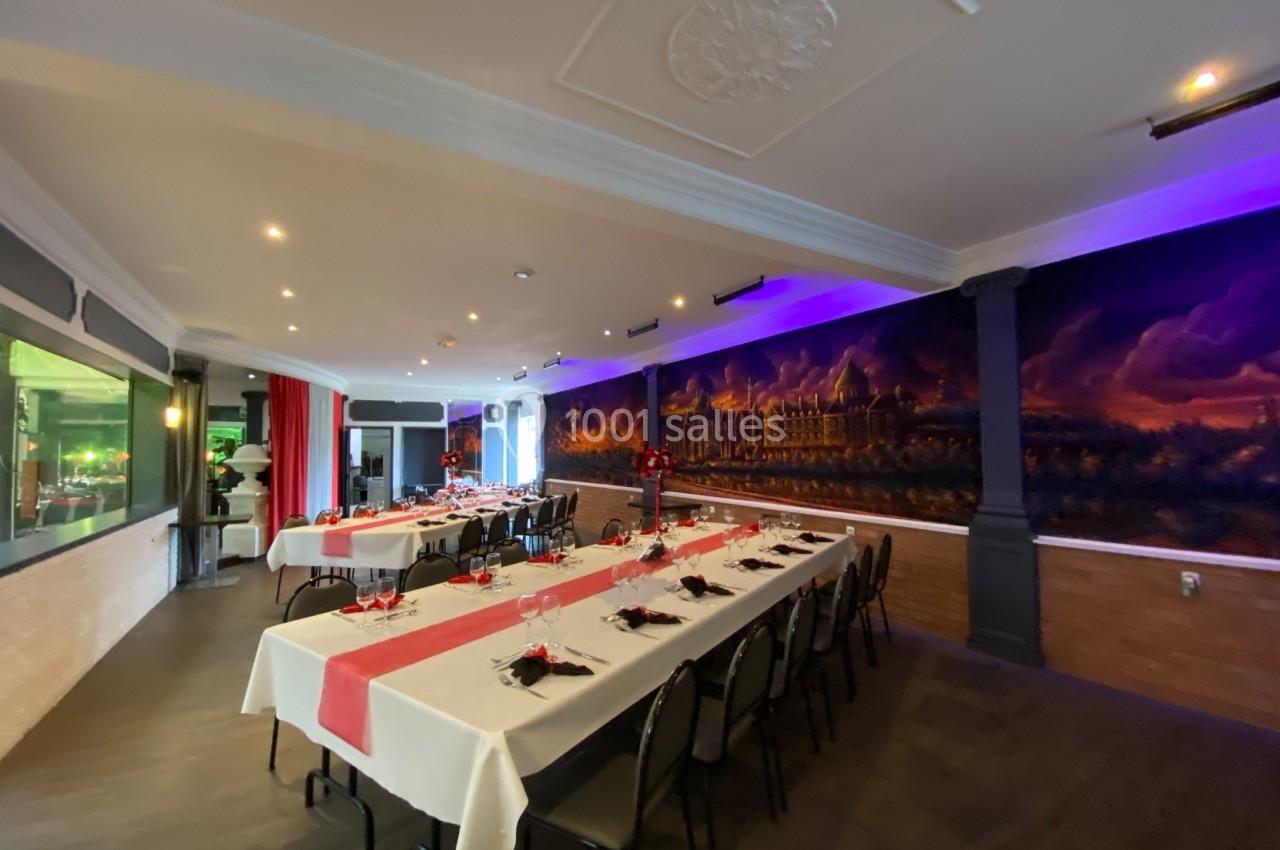 Salle de réception décorée avec des tables dressées, nappes blanches et rouges, et une fresque murale en arrière-plan.