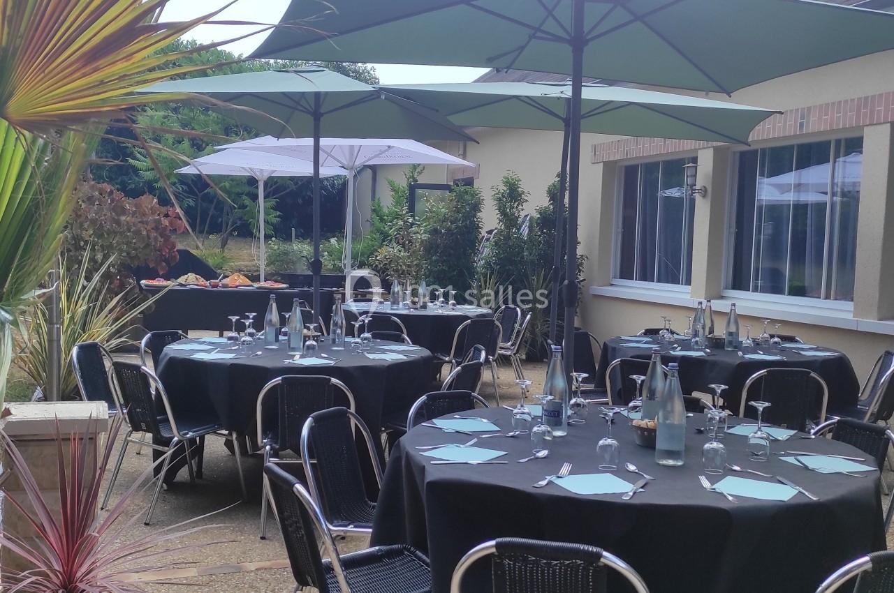 Terrasse aménagée avec des tables rondes dressées, des parasols verts et un buffet en arrière-plan.