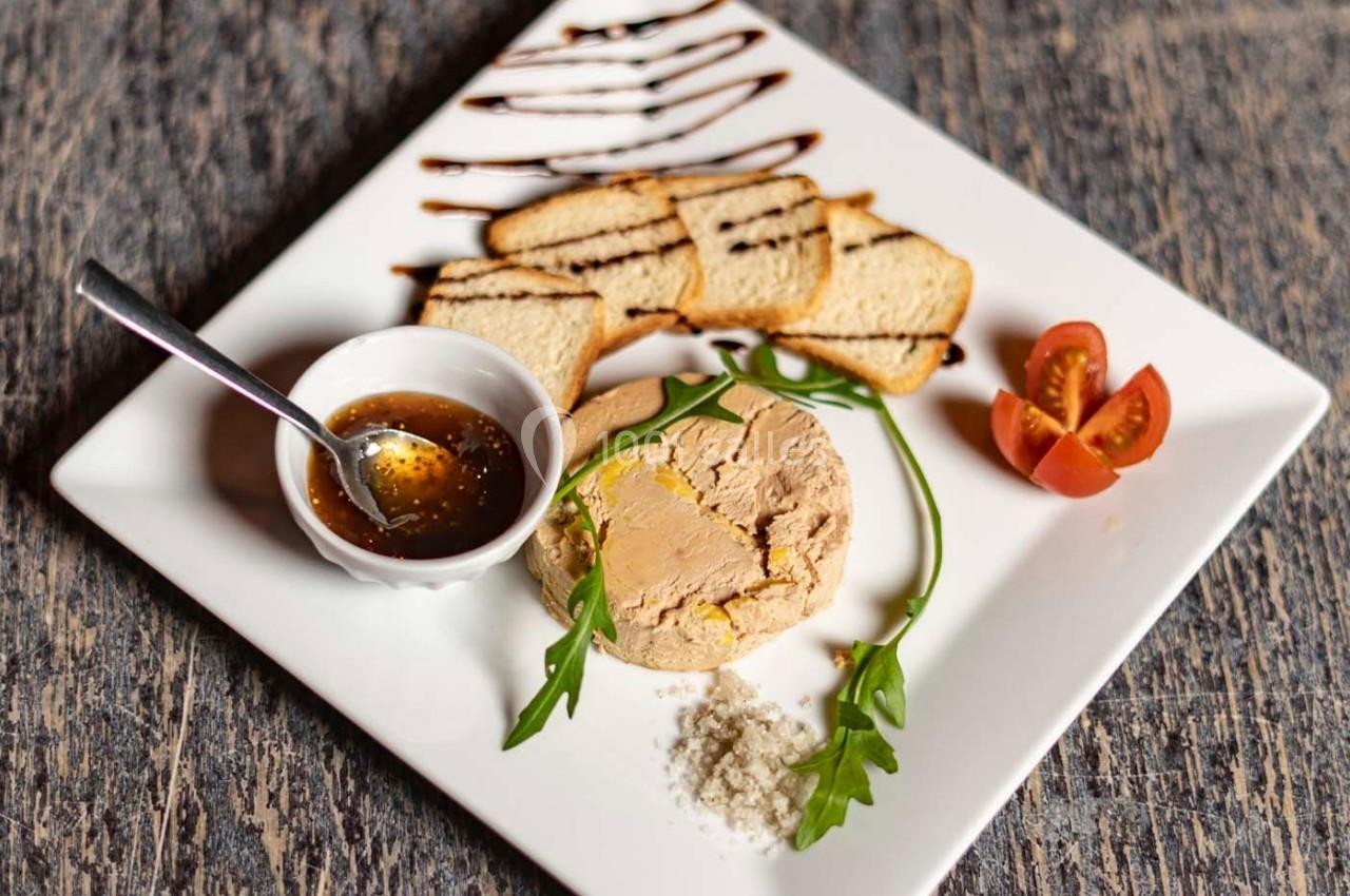 Assiette avec foie gras, toasts, sauce dans un ramequin, tomates cerises et décoration de roquette et balsamique.