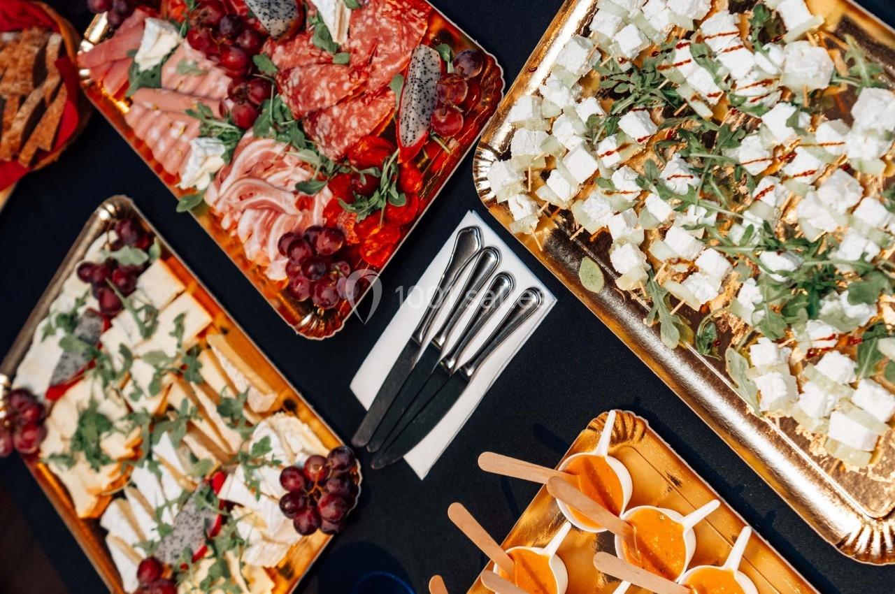 Plateaux garnis de charcuterie, fromages, raisins, et verrines disposés sur une table noire avec des couteaux.