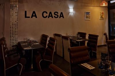 Salle de restaurant avec des tables dressées, des chaises en cuir marron et une enseigne murale ’LA CASA’.