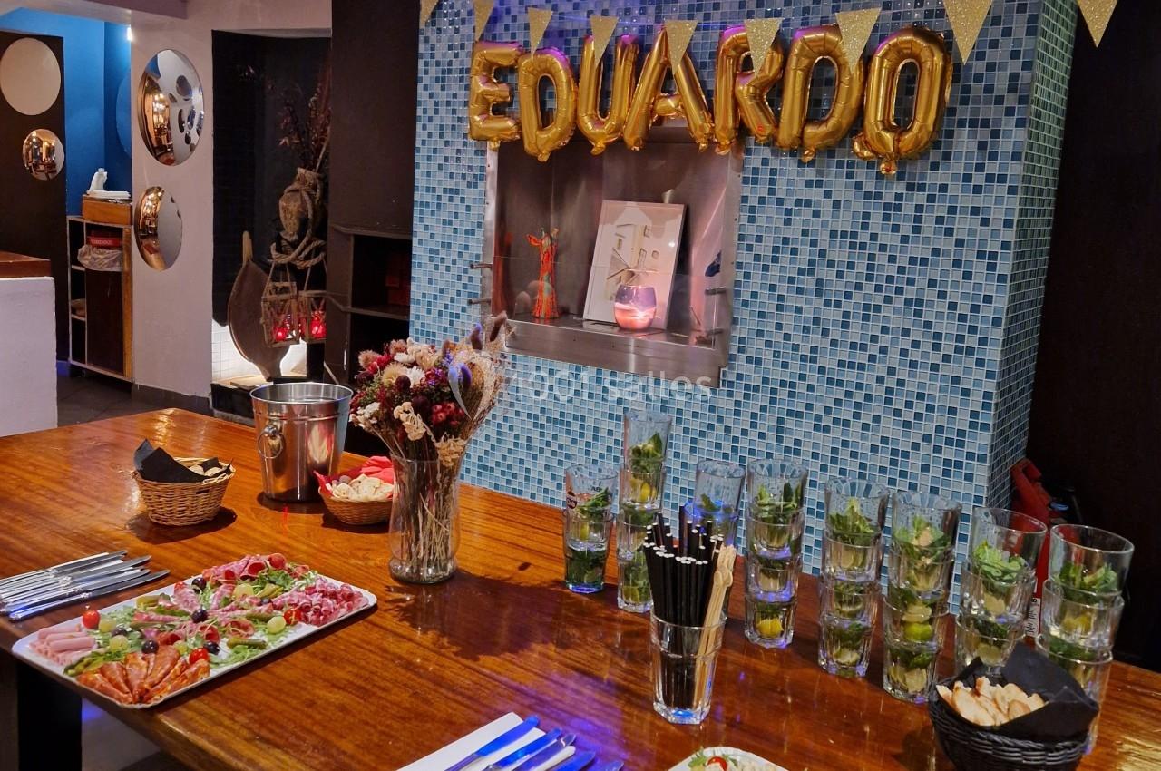 Table décorée pour une fête avec des cocktails, des plats apéritifs et des ballons formant le nom ’Eduardo’.