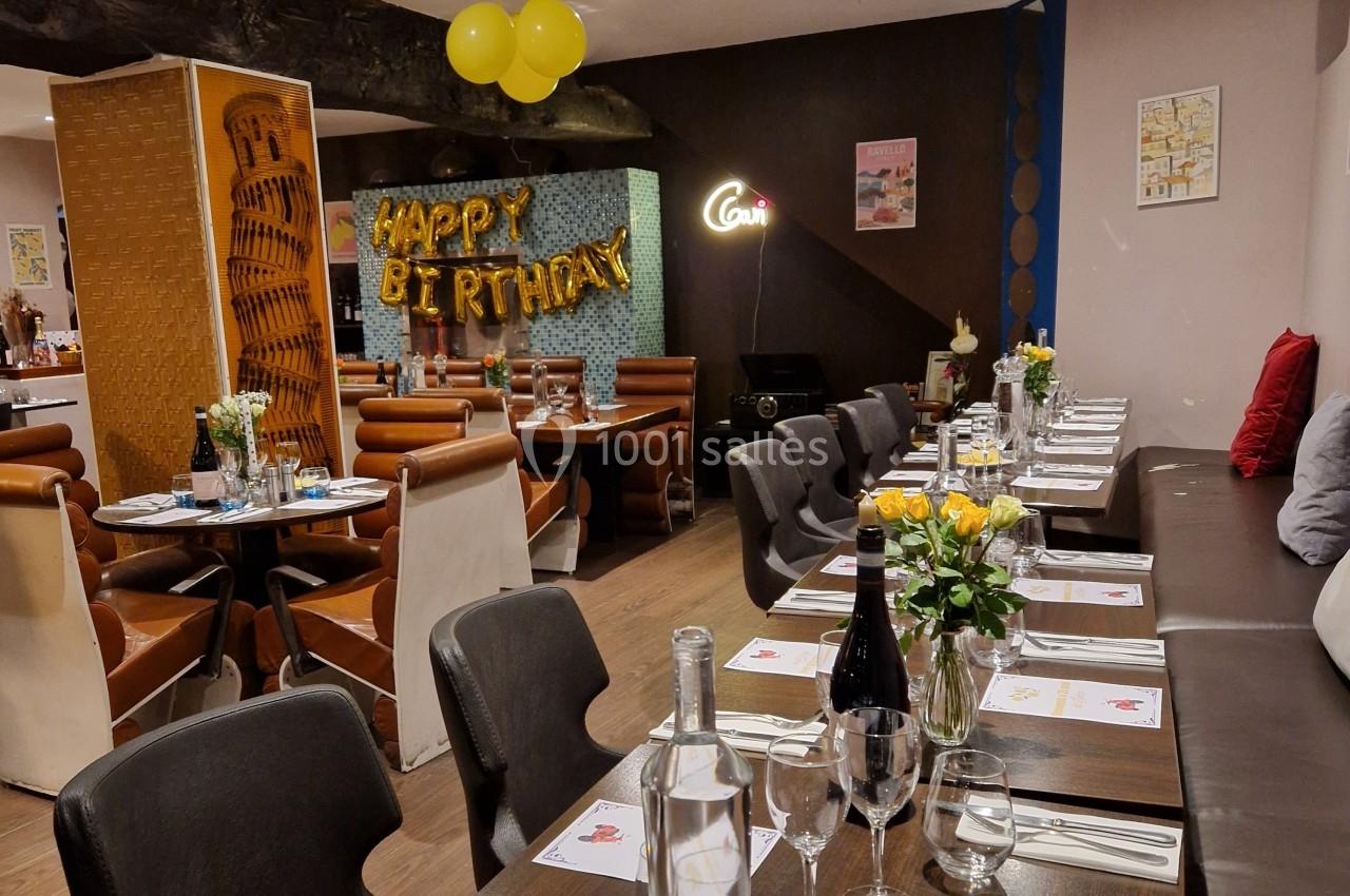 Salle de restaurant décorée pour un anniversaire, avec tables dressées, ballons et guirlande ’Happy Birthday’.